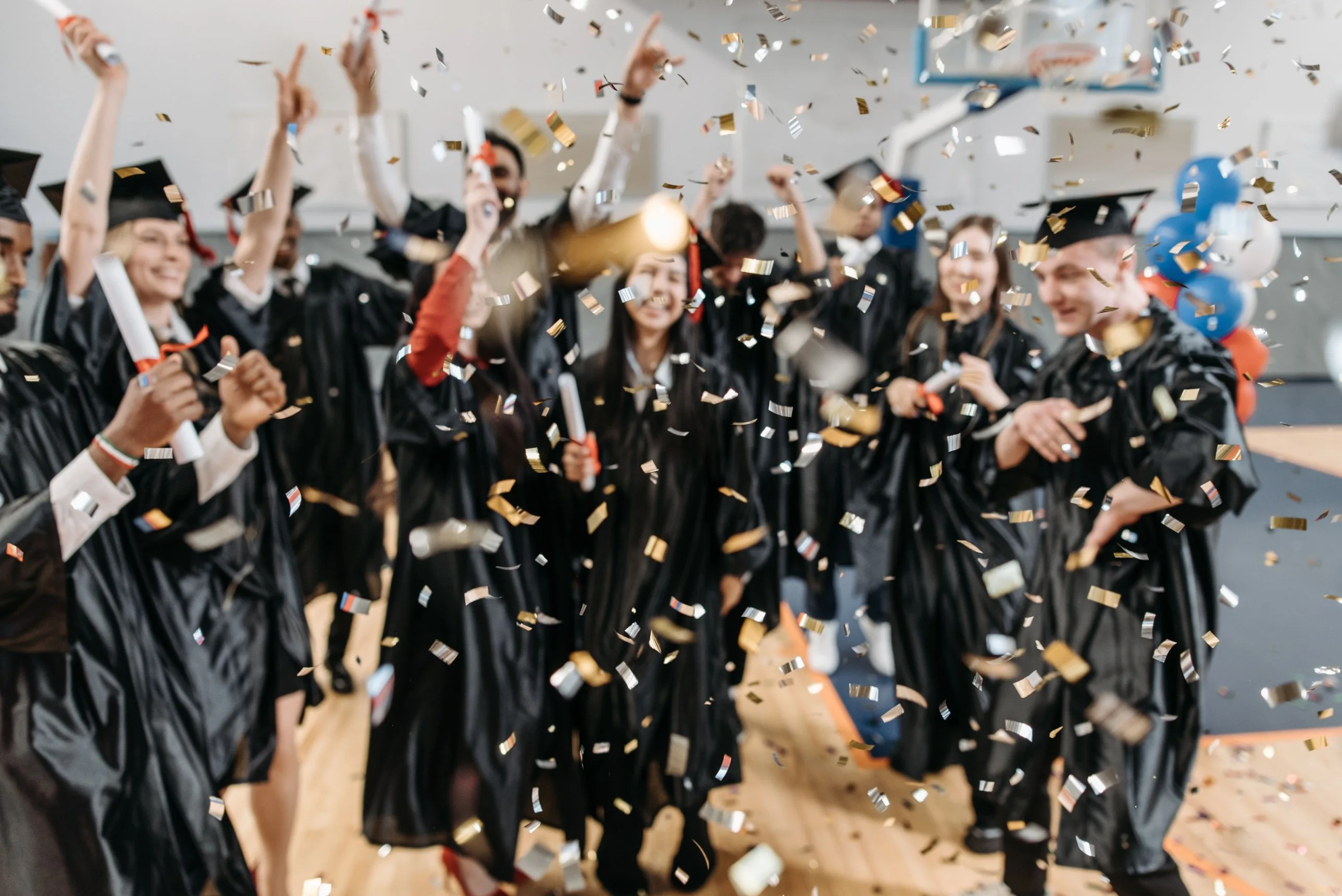 Graduates in gowns celebrating under falling gold confetti